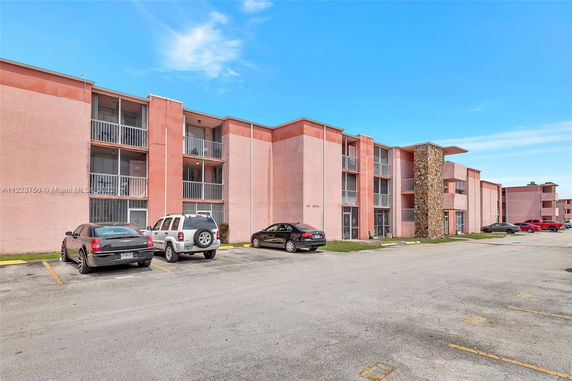 Front view of a multi-story residential building with parking area in front.