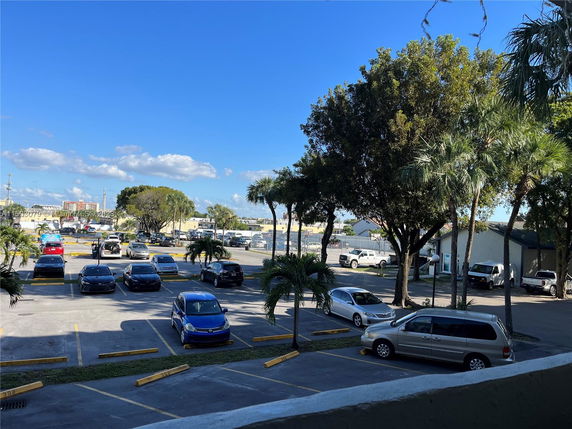 View of a parking lot with several cars and trees nearby.