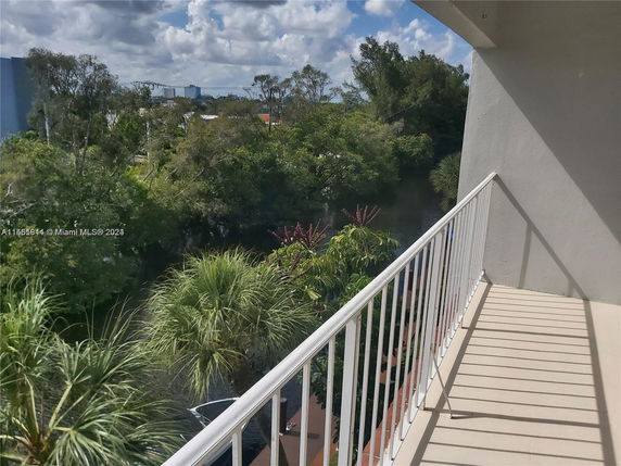 View from a balcony overlooking lush greenery and distant cityscape under a partly cloudy sky.