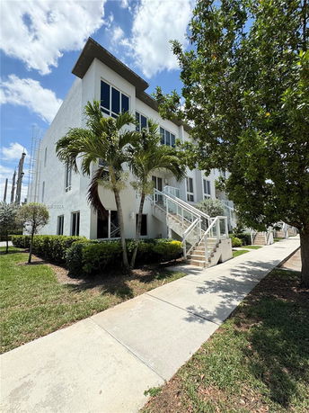 Front view of a modern multi-story white building with large windows and an external staircase.