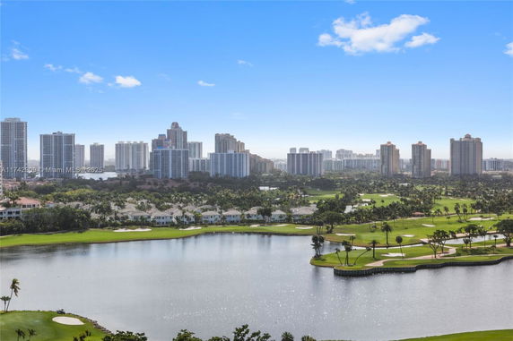 Panoramic view of city skyline with high-rise buildings and a golf course by a water body.
