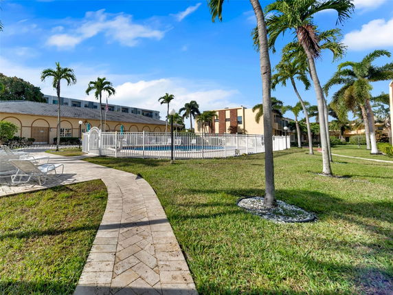 Outdoor swimming pool area fenced and surrounded by grass and palm trees.
