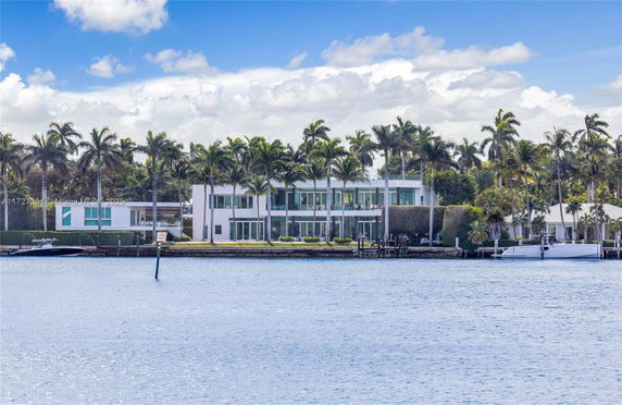 View of a modern waterfront house with palm trees and boats.