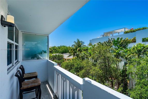 Balcony view with chairs overlooking trees and neighboring buildings.