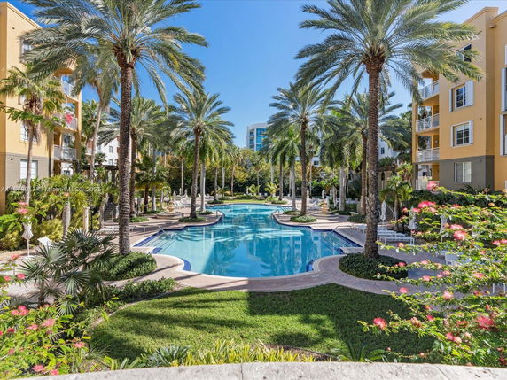 Outdoor swimming pool area surrounded by palm trees and residential buildings.