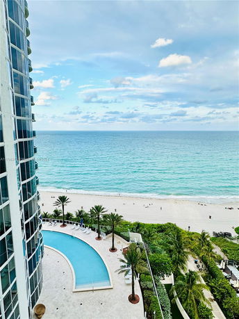 View of ocean and beach from a high-rise building with a swimming pool.