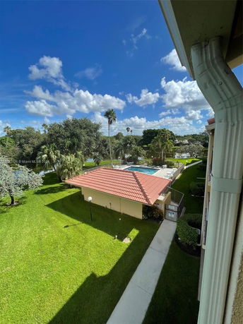 View of a residential area with a swimming pool and green lawn, surrounded by trees.