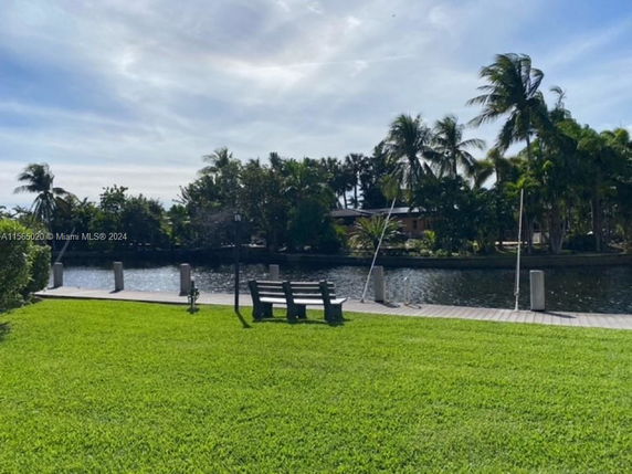 View of a grassy area with a wooden bench overlooking a canal lined with palm trees.