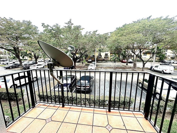 View from a balcony overlooking a parking area with trees and residential buildings.