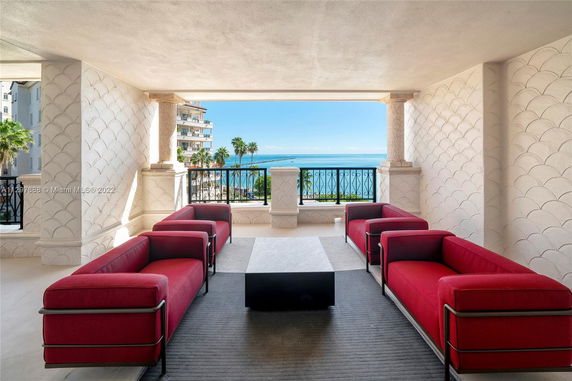 Covered terrace with red sofas and a view of the ocean and nearby buildings.
