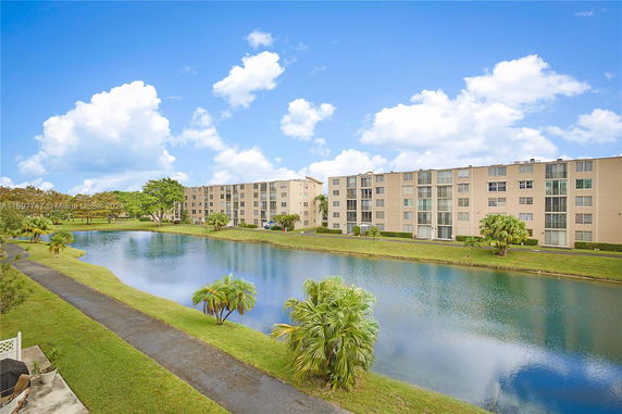 View of multiple residential buildings with a pond and pathways in the foreground.