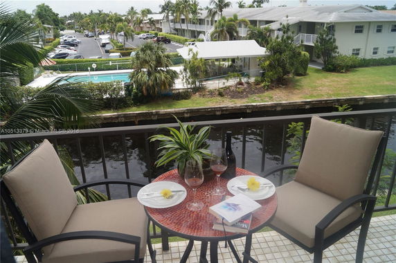 View from a balcony overlooking a pool and parking area of an apartment complex.