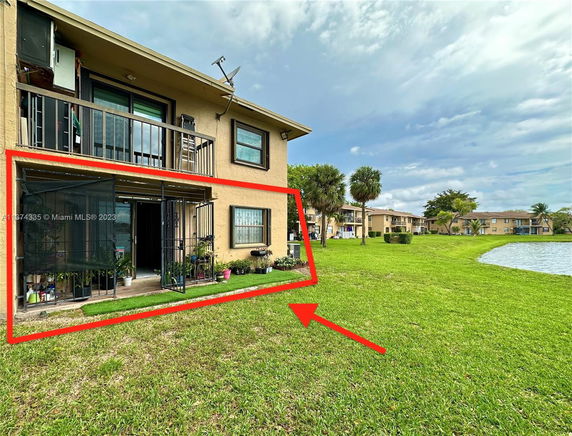 View of a two-story residential building with a balcony, adjacent to a grassy area and a water body.