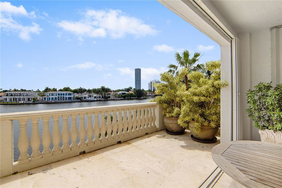Balcony view overlooking a body of water with distant buildings and palm trees.
