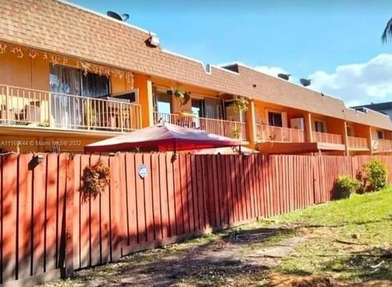 Front view of a two-story apartment building with balconies and a wooden fence.