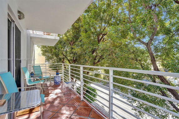 Balcony view with chairs and railing overlooking trees and street.