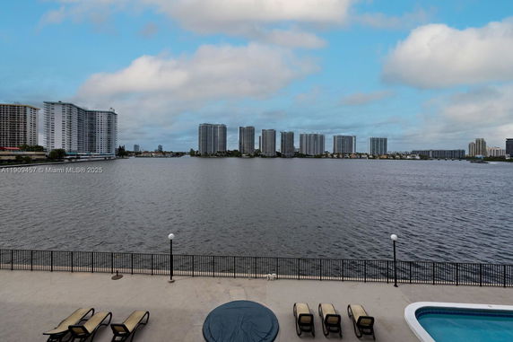 Waterfront view with high-rise buildings in the distance and a swimming pool with loungers in the foreground.