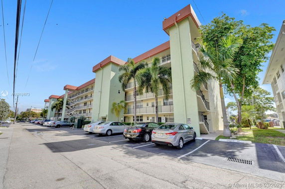 Front view of a multi-story apartment building with balconies and parking spaces.