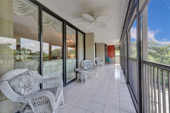 Wide angle view of a modern enclosed balcony with wicker furniture.