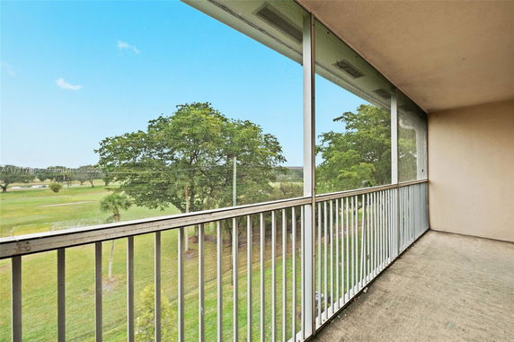 View from a screened balcony overlooking a grassy area with trees.