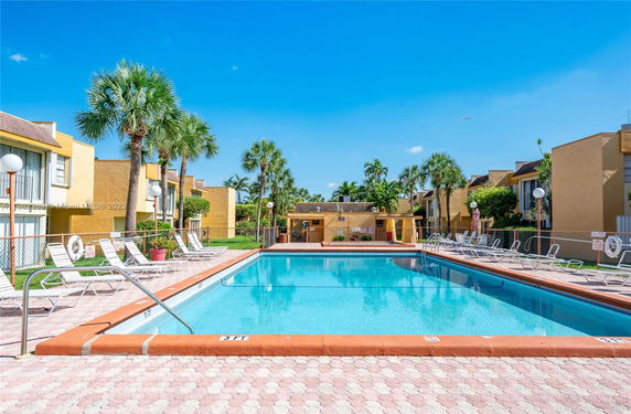 Outdoor swimming pool area with adjacent buildings and palm trees.