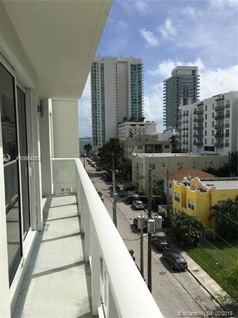 View from a balcony overlooking a street with multiple high-rise buildings and a partly cloudy sky in the background.