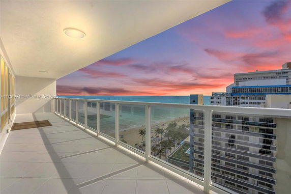 Wide-angle view from a balcony overlooking the ocean and nearby buildings at sunset.
