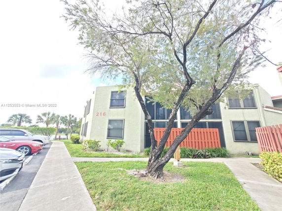 Front view of a two-story residential building with a concrete pathway and tree in the foreground.