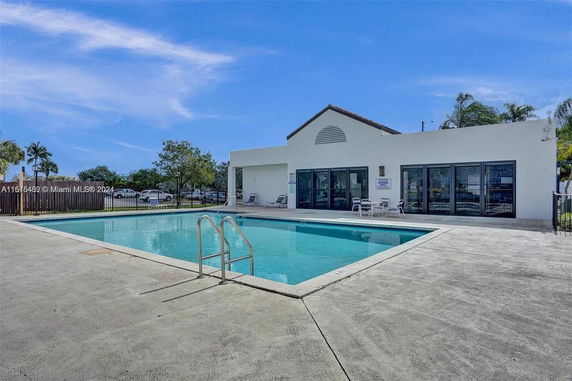 Swimming pool area adjacent to a white building with large windows.