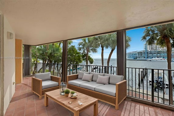 Covered outdoor area with seating overlooking water and palm trees.