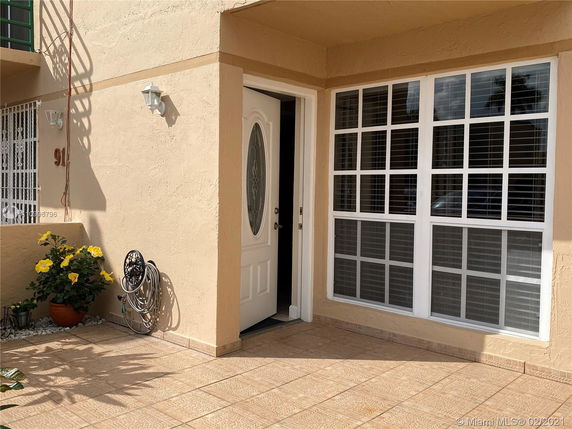 Front view of a house entrance with a white door and large window with shutters.