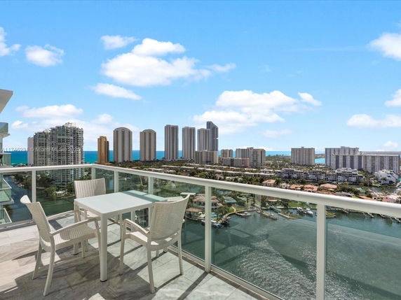 Panoramic view of a cityscape with high-rise buildings and a body of water, as seen from a balcony.