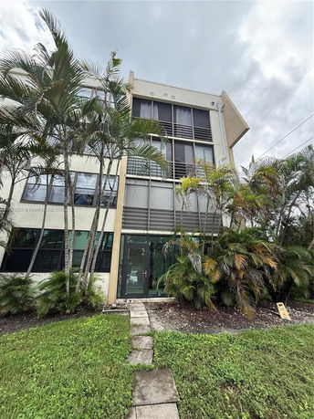 Front view of a multi-story building with large windows and surrounding palm trees.