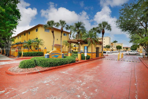 Front view of a multi-story residential building with palm trees and a gated entrance.