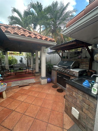 Outdoor patio area with a barbecue setup and seating under a tiled roof structure.