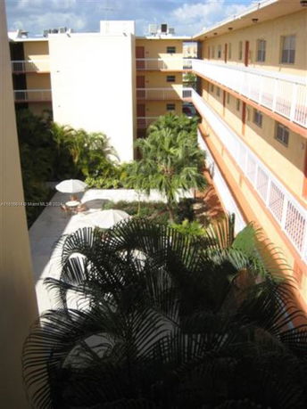 View of a multi-story building with balconies overlooking a courtyard with greenery.