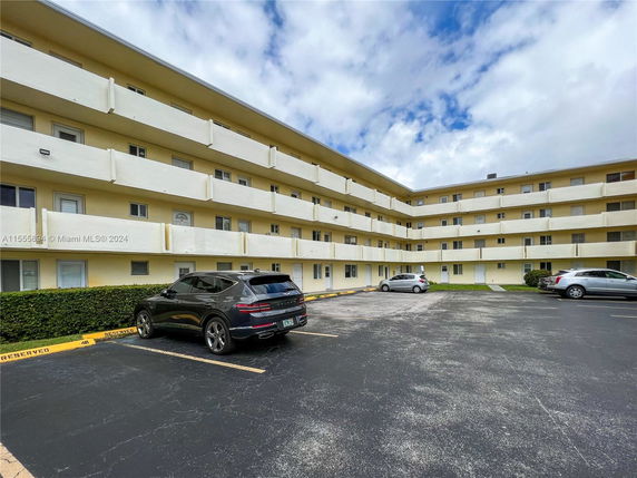 Outdoor parking area in front of a multi-story building with balconies.