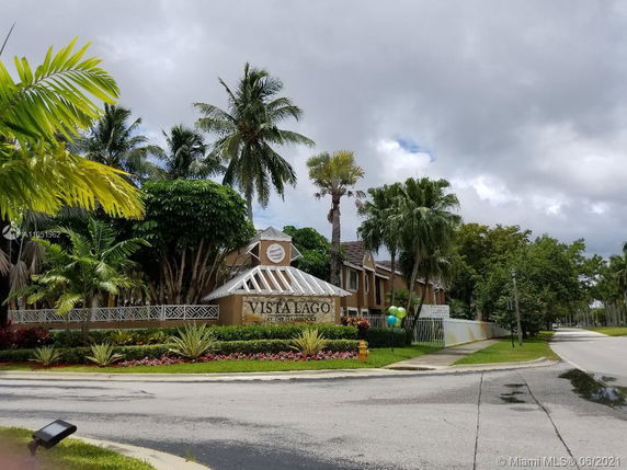 Front view of a residential complex with a sign that reads 'Vista Lago', surrounded by palm trees and landscaping.