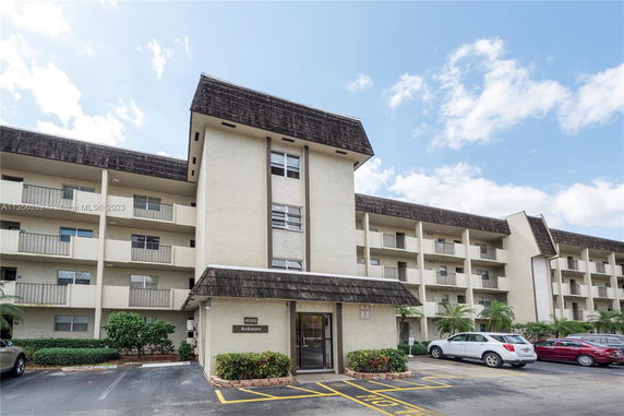 Front view of a multi-story apartment building with balconies and a parking area.