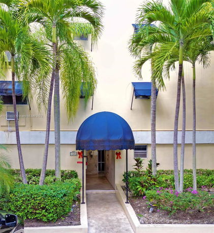 Front view of a building entryway with blue canopy and palm trees.