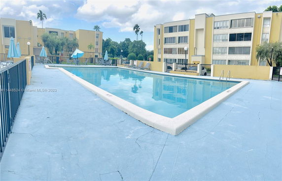 Outdoor swimming pool area in front of a multi-story apartment building.