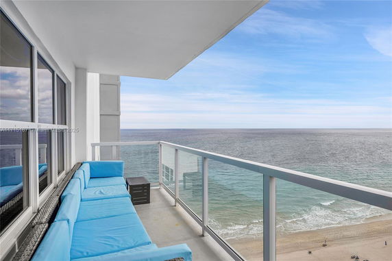 View of the ocean and beach from a balcony with blue cushioned seating.
