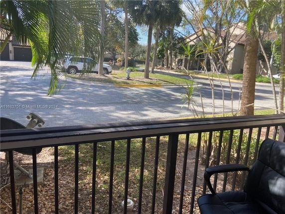 View of a residential street through a terrace with railing and a chair.