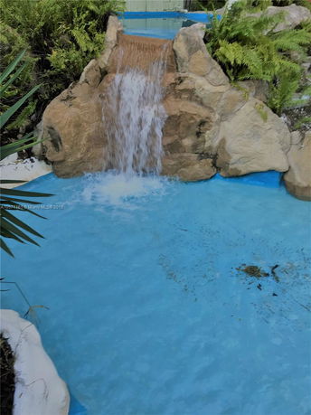 Artificial waterfall flowing into a blue pool, surrounded by rocks and greenery.