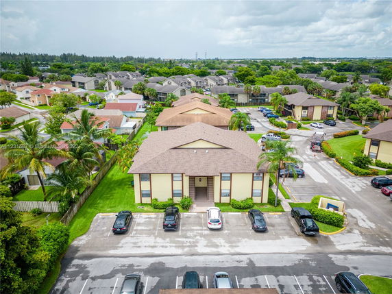 Aerial view of residential buildings with parking area and surrounding neighborhood.