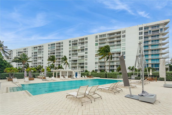 Outdoor swimming pool area in front of a multi-story residential building.