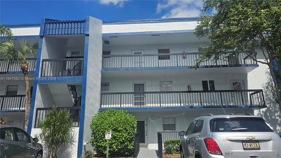 Front view of a multi-story building with balconies and a parking area.