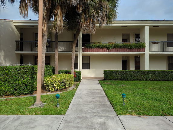 Front view of a two-story building with a balcony and greenery.