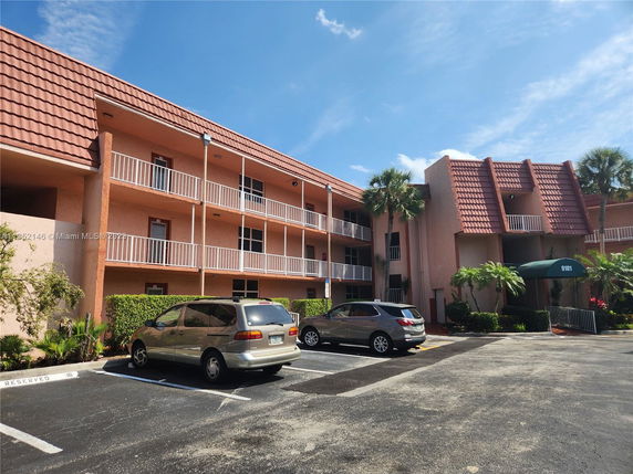 Front view of a multi-story building with balconies and a parking area.