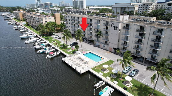 Aerial view of a multi-story waterfront building with a swimming pool and adjacent docks for boats.
